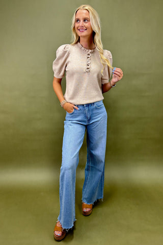 Woman wearing a beige blouse and blue jeans against a green background