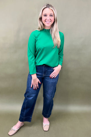 Woman wearing a green top and blue jeans against a plain background