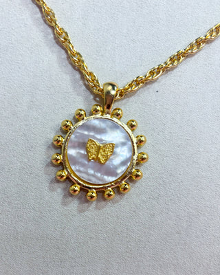 Gold necklace with a round pendant featuring a butterfly design on a light gray background