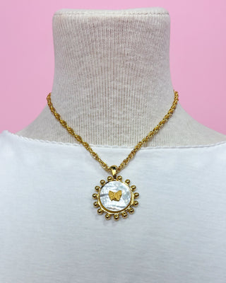 Gold necklace with a pendant on a mannequin against a pink background