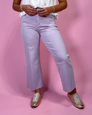 Person wearing light purple jeans and white sneakers on a pink background