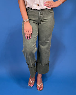 A model wearing olive green cropped jeans with frayed ruffle trim at the hem, paired with a white top