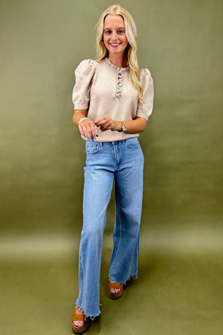 Woman wearing a beige blouse and blue jeans against a green background