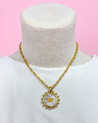 Gold necklace with a circular pendant on a mannequin against a pink background