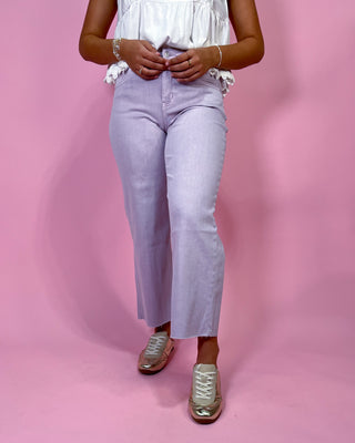 Person wearing light purple jeans and a white top on a pink background