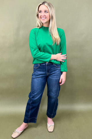 Woman wearing a green top and blue jeans against a beige background
