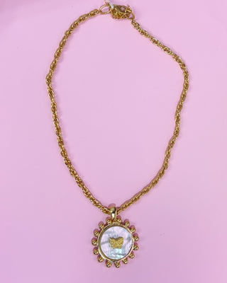 Gold necklace with a circular pendant on a pink background