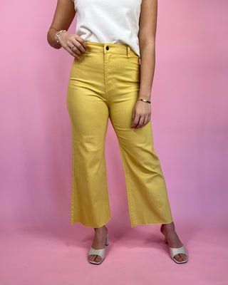 Person wearing yellow pants and a white top on a pink background