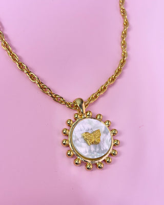 Gold necklace with a circular pendant featuring a butterfly design on a pink background