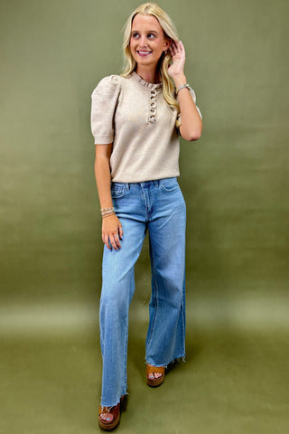 Woman wearing a beige top and blue jeans against a green background