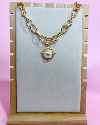 Gold chain necklace with a pearl pendant on a wooden stand against a pink background