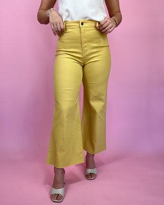 Person wearing yellow pants and a white top against a pink background