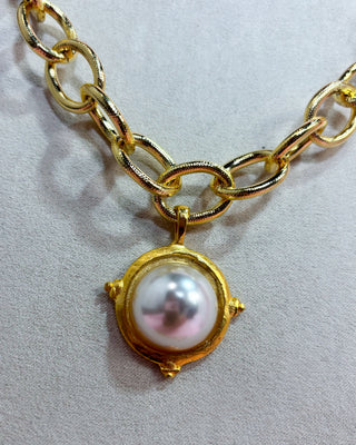 Gold chain bracelet with a pearl pendant on a light gray background