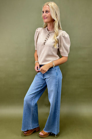 Woman wearing a beige top and blue jeans against a green background