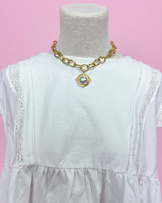 White dress with gold chain necklace on a mannequin against a pink background