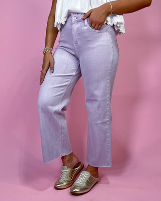 Person wearing light purple jeans and gold shoes on a pink background