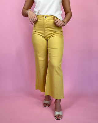 Person wearing yellow pants and a white top against a pink background