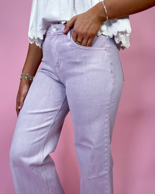 Person wearing light purple jeans and a white blouse against a pink background