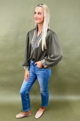 Woman wearing a green blouse, blue jeans, and a plaid shirt underneath against a green background