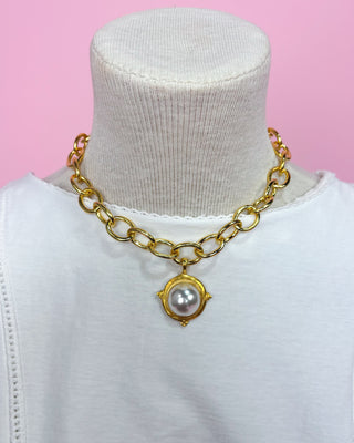 Gold chain necklace with a pearl pendant on a mannequin against a pink background