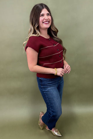 Woman wearing a red sweater with black buttons and blue jeans against a green background