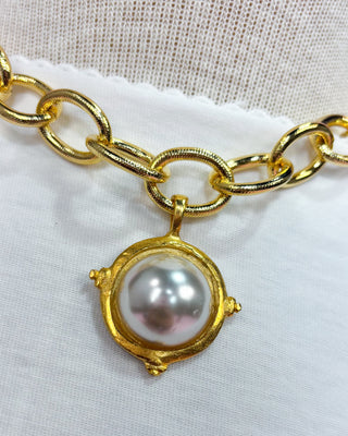 Gold chain bracelet with a pearl pendant on a white fabric background