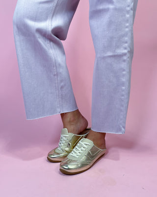 Gold sneakers worn with light blue jeans on a pink background