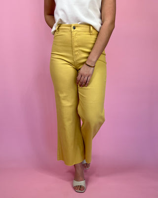 Person wearing yellow pants and a white top on a pink background