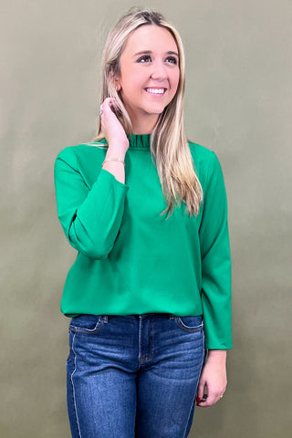 Woman wearing a green top and blue jeans against a beige background