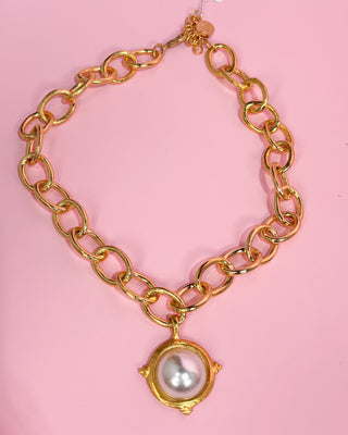 Gold chain necklace with a pearl pendant on a pink background