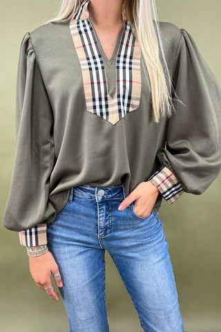 Person wearing a green blouse with plaid accents and blue jeans against a plain background