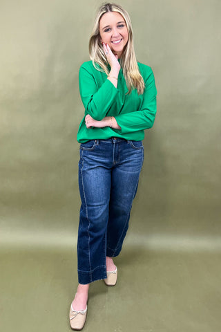 Woman wearing a green sweater and blue jeans against a beige background