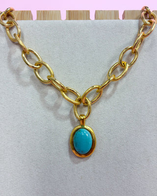 Gold chain necklace with a turquoise pendant on a light gray background