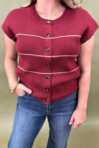 Person wearing a red knitted cardigan with white stripes and blue jeans against a beige background