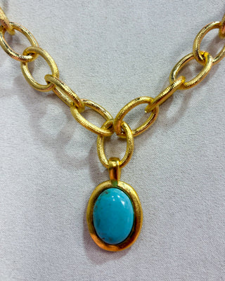 Gold chain necklace with a turquoise pendant on a light gray background