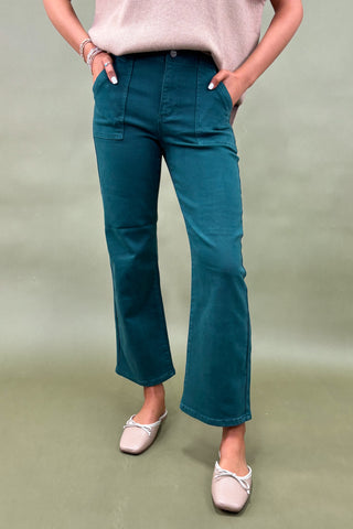 Person wearing teal pants and a light pink top on a green background