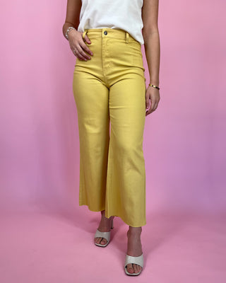 Person wearing yellow pants and a white top on a pink background