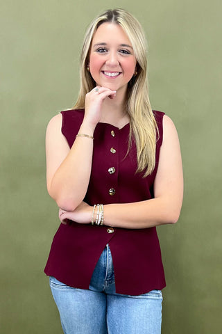 Woman wearing a burgundy sleeveless top with buttons against a green background