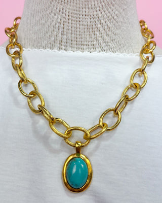Gold chain necklace with a turquoise pendant on a mannequin.