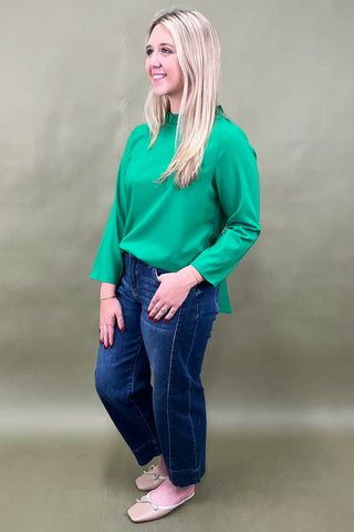 Woman wearing a green top and blue jeans against a plain background