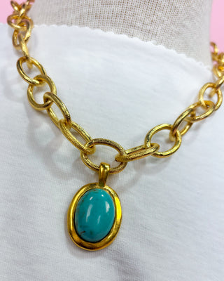 Gold chain necklace with a turquoise pendant on a mannequin.