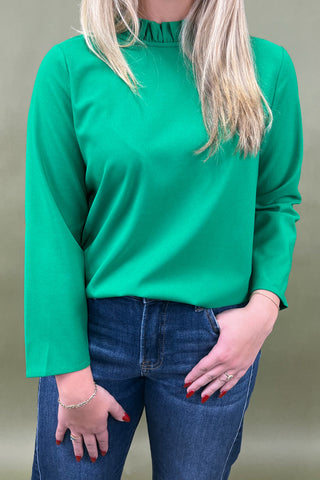 Person wearing a green long-sleeve top and blue jeans against a neutral background