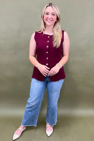 Woman wearing a burgundy sleeveless top and blue jeans against a green background