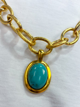 Gold chain necklace with a turquoise pendant on a white background