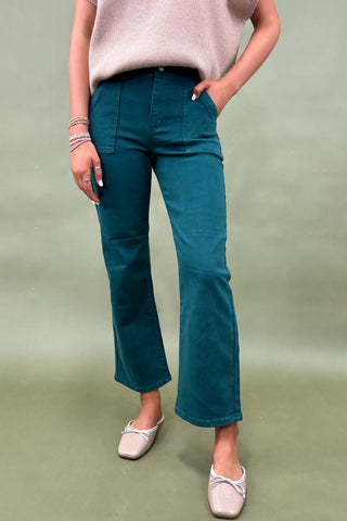 Person wearing teal pants and a beige top on a plain background