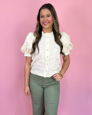 Woman wearing a white lace blouse and green pants against a pink background