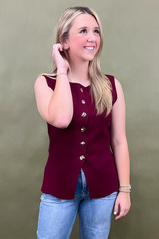 Woman wearing a burgundy sleeveless top with buttons against a green background