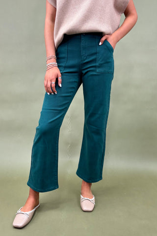 Person wearing teal pants and a light pink top on a green background