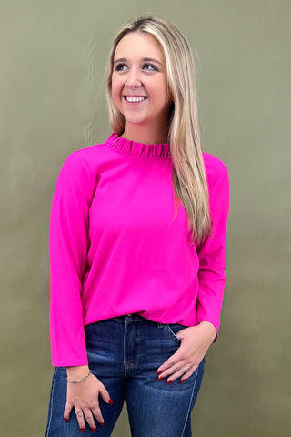 Woman wearing a bright pink long-sleeve top and blue jeans against a green background