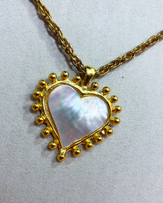 Woman wearing a gold necklace with a heart-shaped pendant on a white background